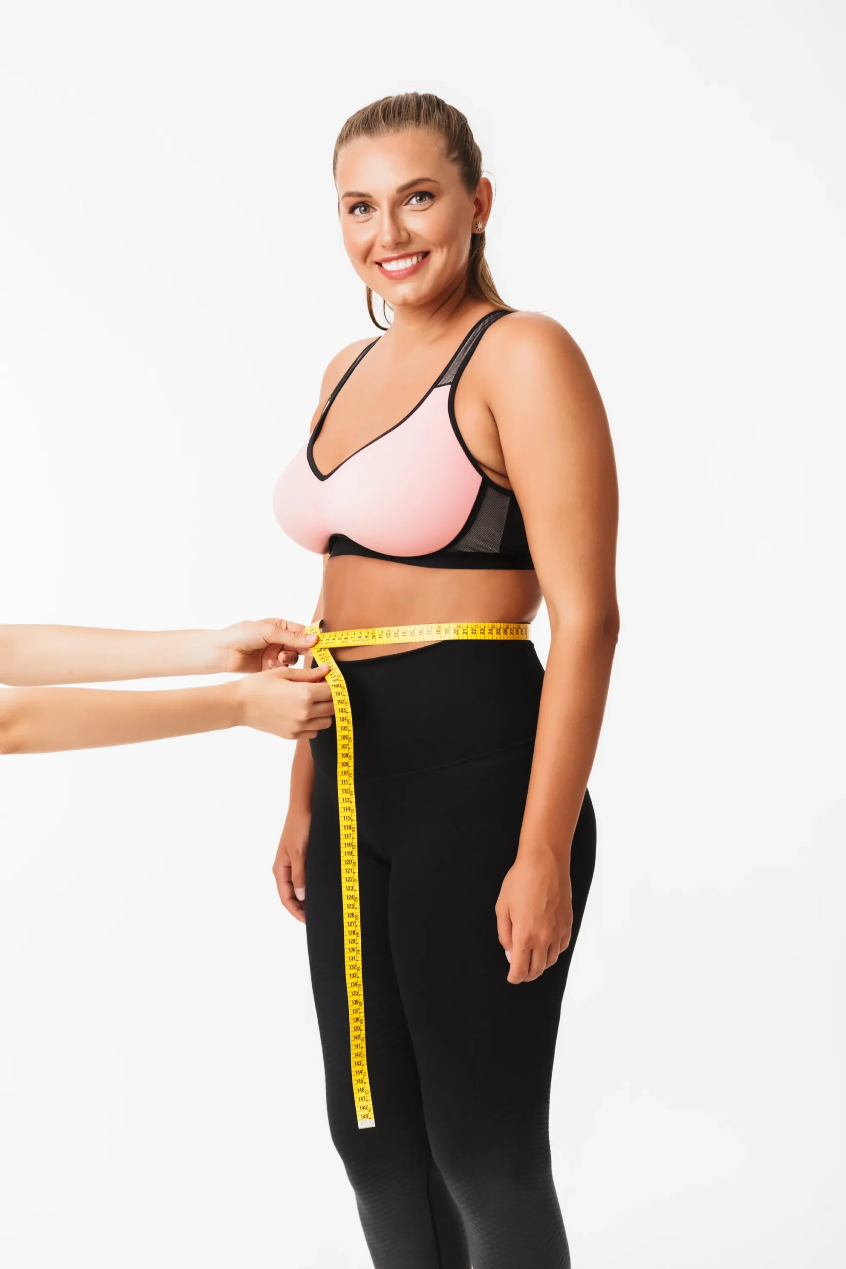 GLP-1 Therapy beautiful smiling girl with excess weight sporty top measuring waist while happily looking camera white background scaled