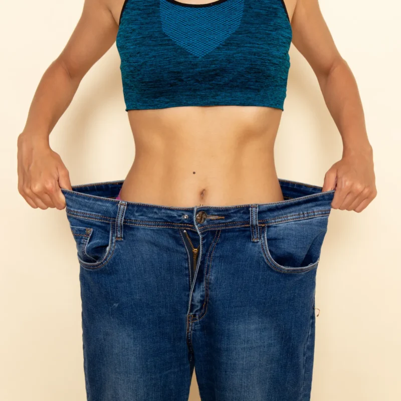 GLP-1 Therapy front view young female with fit body blue shirt jeans light white wall